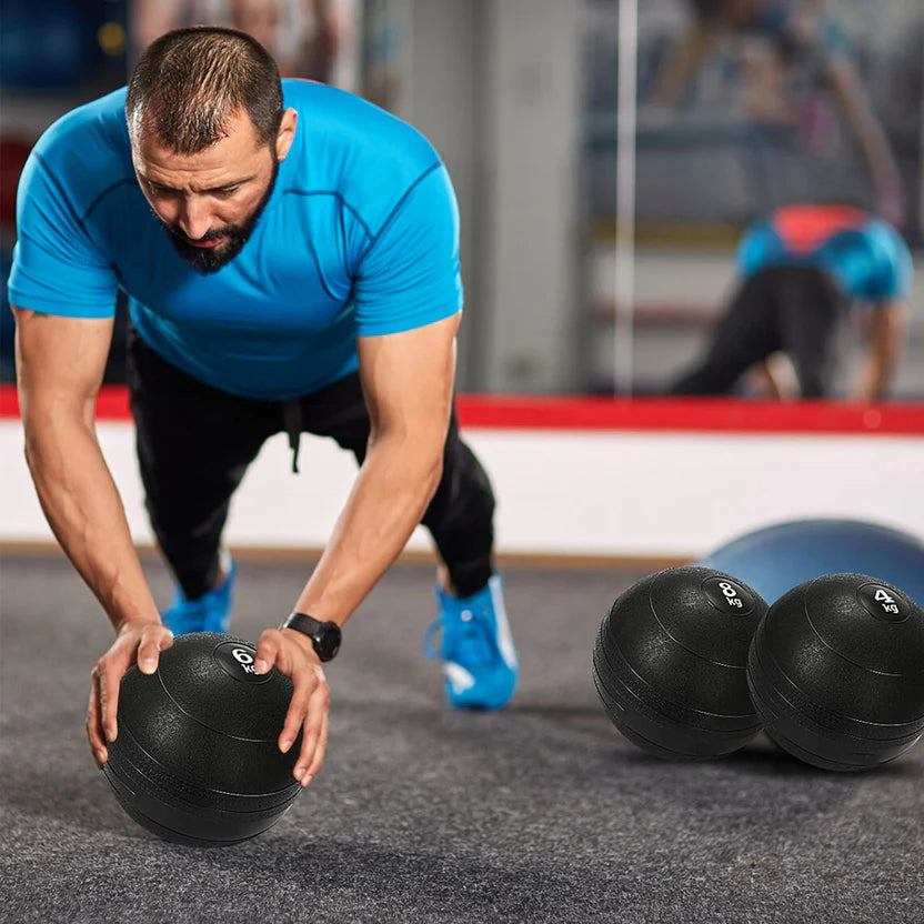 Man in blue shirt and black pants exercising with medicine balls in a gym setting.